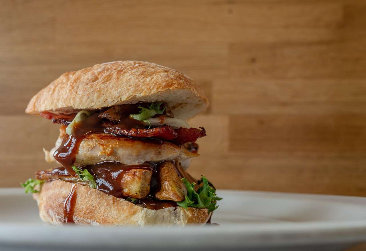 Gourmet sandwich with grilled chicken, bacon, vegetables, and artisan bread on a restaurant plate, representing Catering Kitchen Financing, Restaurant Staffing Financing, Food Distribution Financing, Restaurant Supply Financing, and Drive Thru Technology Financing for restaurants seeking capital to expand operations, improve logistics, hire staff, and modernize customer service systems.