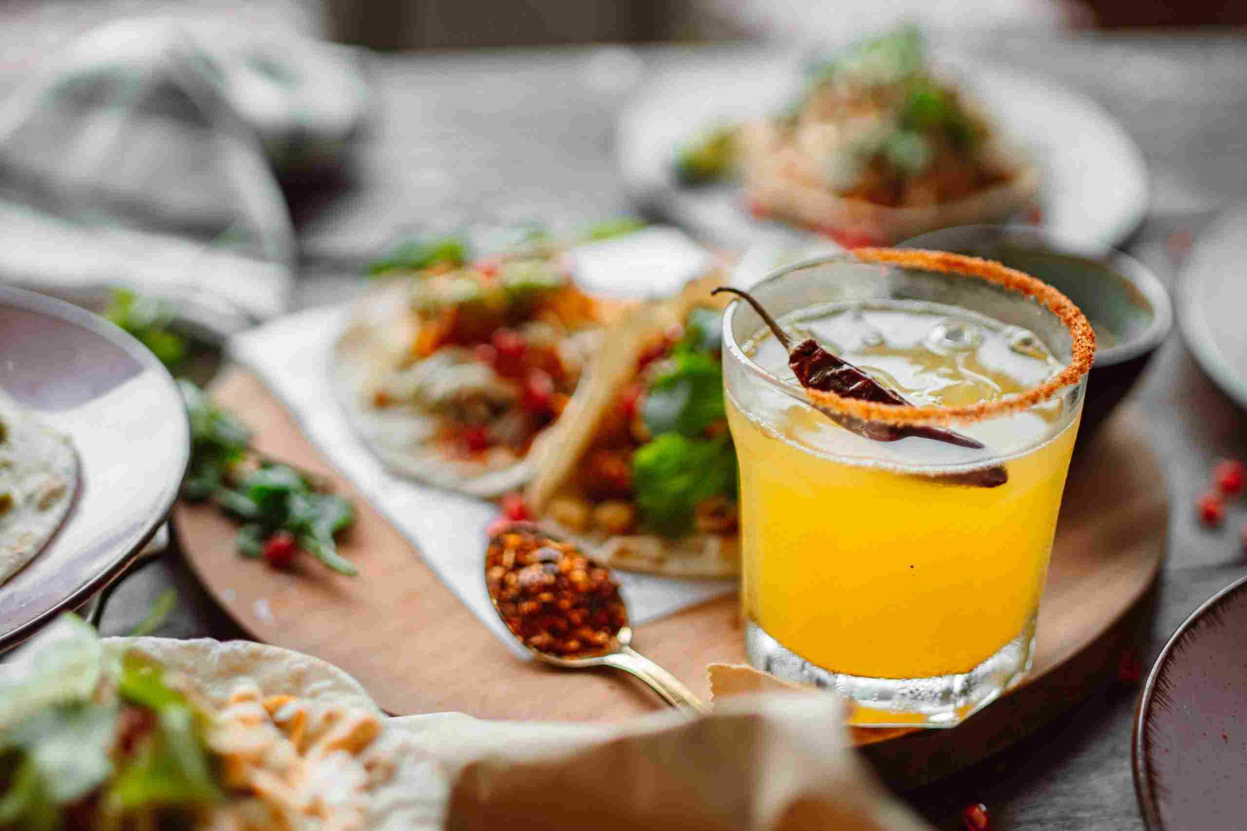 Colorful cocktail served alongside gourmet restaurant dishes, representing Compare Restaurant Loans, Loans for Restaurant Renovations, Restaurant Funding Solutions, Hospitality Payroll Capital, and Catering Business Financing for restaurant owners seeking growth, staffing, renovation, and catering expansion funding.