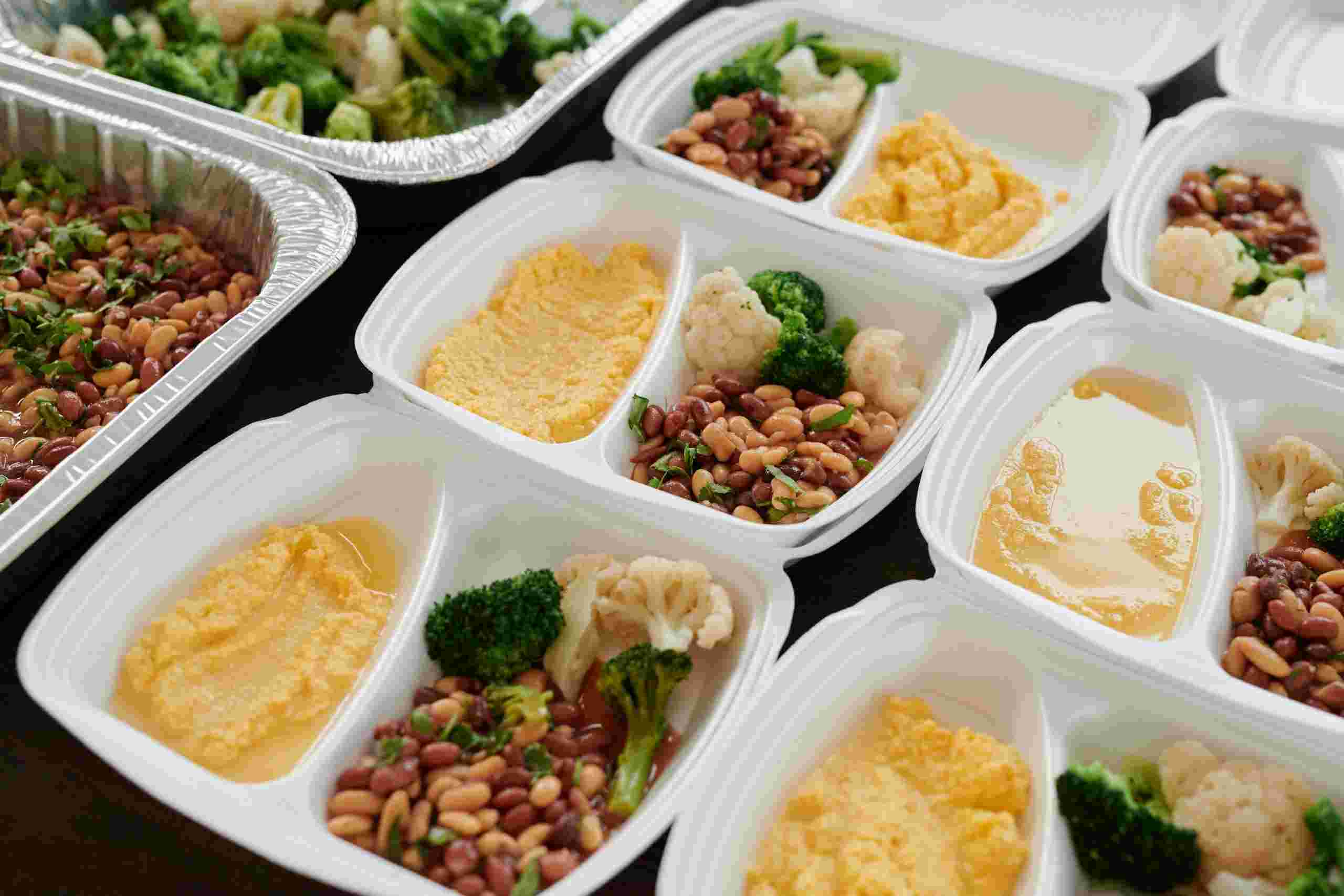 Prepared meal trays filled with vegetables, beans, and hot food portions ready for large-scale food service distribution, representing operations that may utilize Restaurant commercial mortgage, dining room renovation financing, commercial dishwasher financing, and bulk food purchasing financing to support facility ownership, customer area improvements, kitchen efficiency, and large-volume inventory purchases.